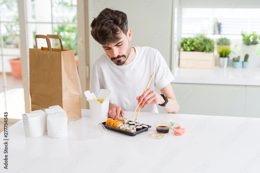 Young man eating sushi asian food and noodles using choopsticks from take away delivery Young man eating sushi asian food and noodles using choopsticks from take away delivery