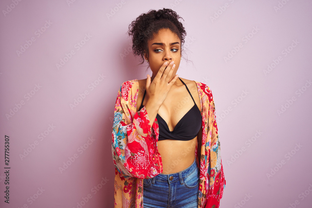 American woman on holiday wearing bikini and colorful dress over isolated pink background bored yawning tired covering mouth with hand. Restless and sleepiness.