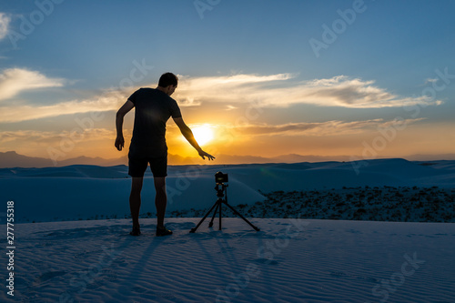 Man photographer with tripod doing time lapse photography with camera in white sands dunes national monument in New Mexico view of sunset