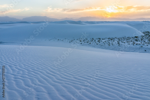 White sands dunes national monument pattern in New Mexico with sun over horizon at sunset with silhouette of Organ Mountains