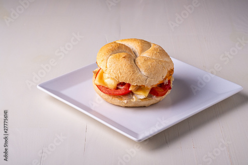 Single homemade burger Vienna Kaiser bread bun bread roll with chicken meat tomato mustard mayonnaise on white square plate background