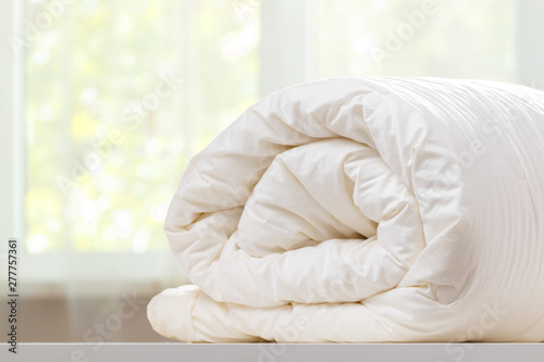 A folded rolls duvet is lying on the dresser against the background of a blurred window. Household.