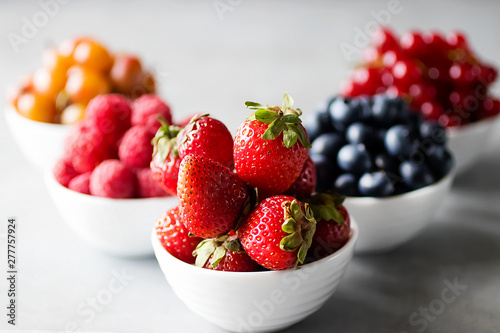 Fresh berries in white bowls on a gray background. Blueberries  strawberry  raspberry  gooseberries and redcurrants.