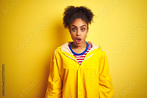 Young african american woman wearing rain coat over isolated yellow background afraid and shocked with surprise expression, fear and excited face. © Krakenimages.com