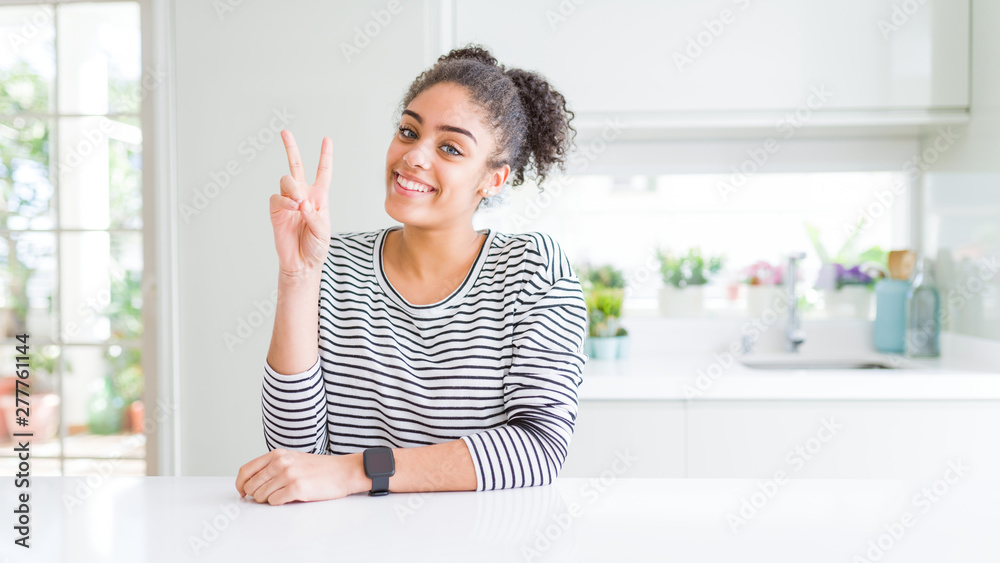 Beautiful african american woman with afro hair wearing casual striped sweater smiling looking to the camera showing fingers doing victory sign. Number two. Beautiful african american woman with afro hair wearing casual striped sweater smiling looking to the camera showing fingers doing victory sign. Number two.