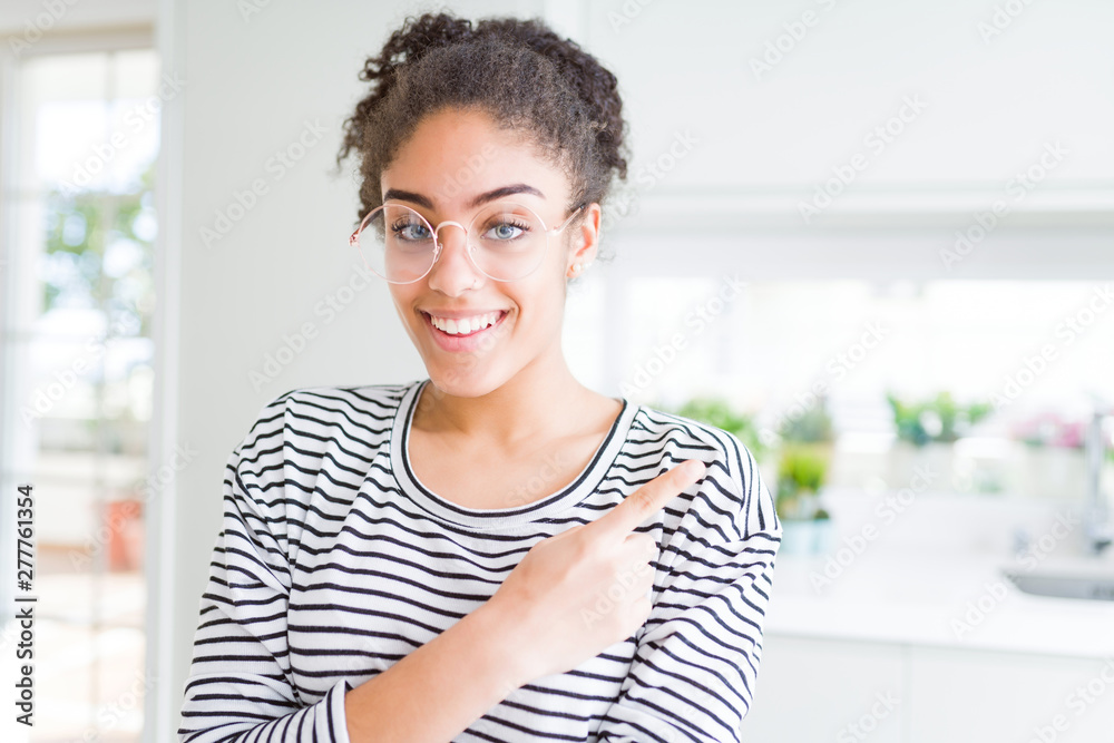 Beautiful young african american woman with afro hair wearing glasses cheerful with a smile of face pointing with hand and finger up to the side with happy and natural expression on face
