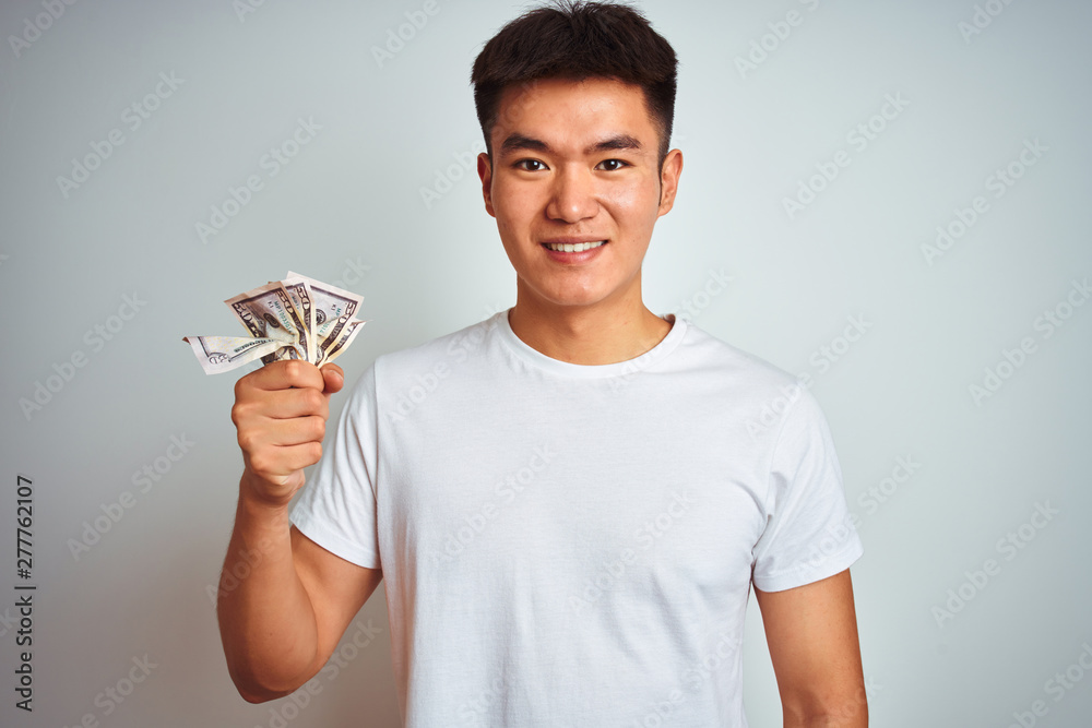 Young asian chinese man holding dollars standing over isolated white background with a happy face standing and smiling with a confident smile showing teeth