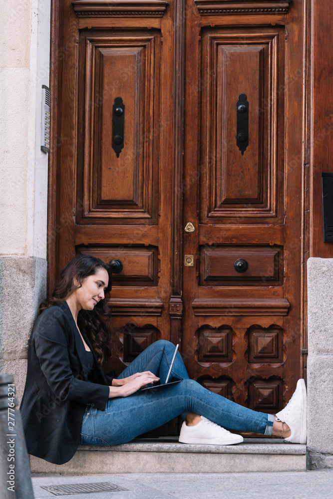 Side view of beautiful woman using digital tablet while relaxing on threshold of old wooden door Side view of beautiful woman using digital tablet while relaxing on threshold of old wooden door