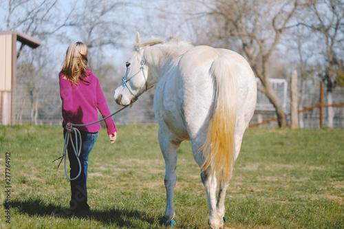 Woman walking gray mare horse through farm grass, equine western lifestyle image.