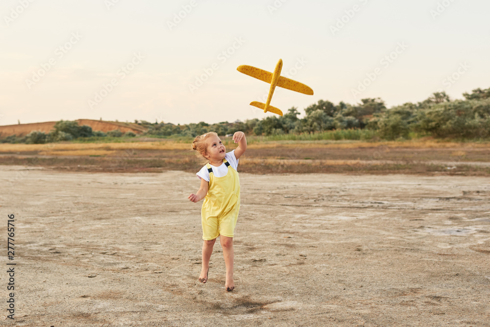 Happy kid girl playing with toy airplane on the beach on sunset