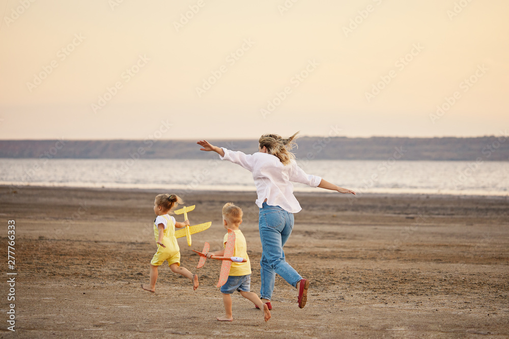 Happy family of mother and two children  launch a kite on nature at sunset. They having fun and running. Straightened their arms like a plane