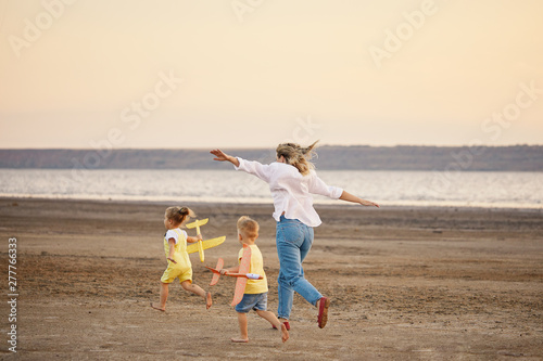 Happy family of mother and two children launch a kite on nature at sunset. They having fun and running. Straightened their arms like a plane