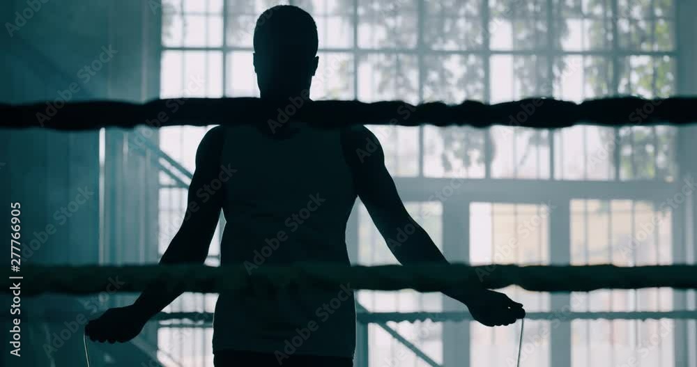 Cinematic slow motion shot of a professional young muscular african man is jumping rope before shadow boxing work out in a ring. Cinematic slow motion shot of a professional young muscular african man is jumping rope before shadow boxing work out in a ring.