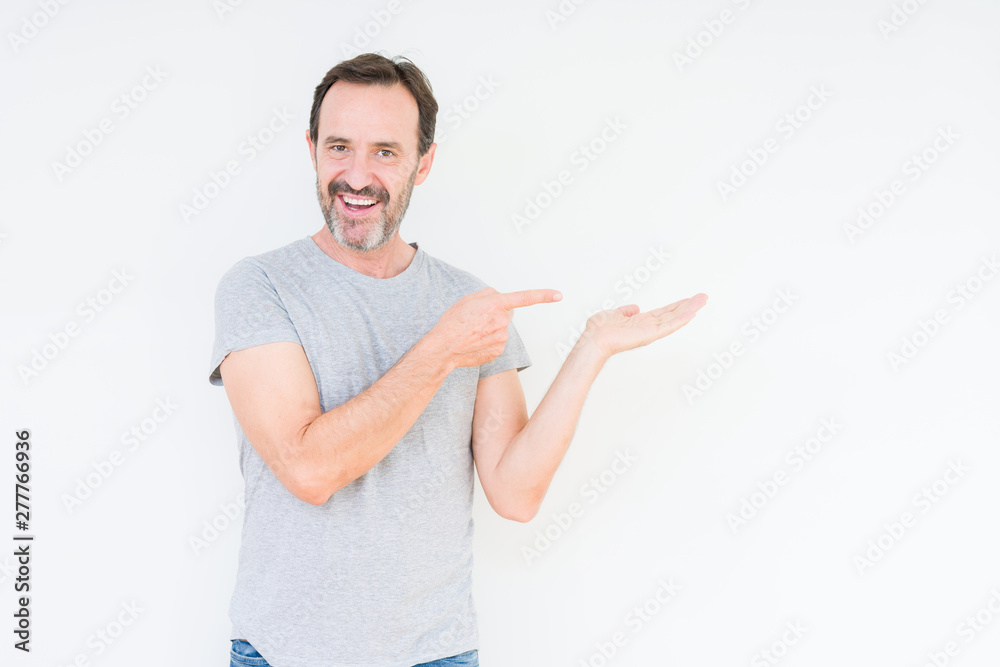 Handsome senior man over isolated background amazed and smiling to the camera while presenting with hand and pointing with finger.