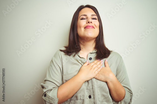 Young beautiful brunette woman wearing green shirt over isolated background smiling with hands on chest with closed eyes and grateful gesture on face. Health concept. © Krakenimages.com