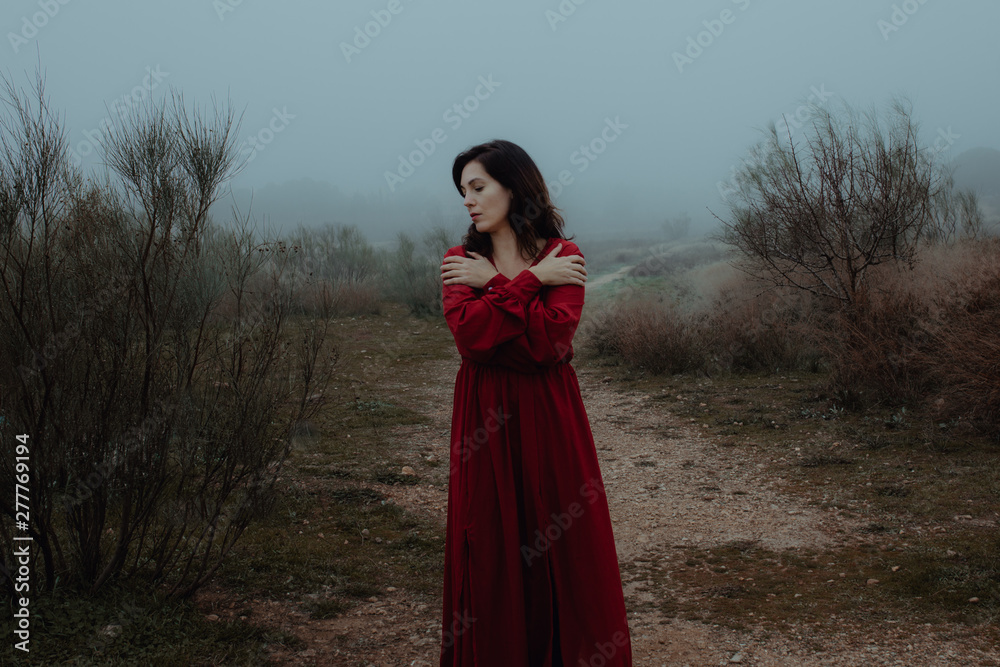 Dreamy woman in red dress walking along empty road of hazed mysterious terrain Dreamy woman in red dress walking along empty road of hazed mysterious terrain