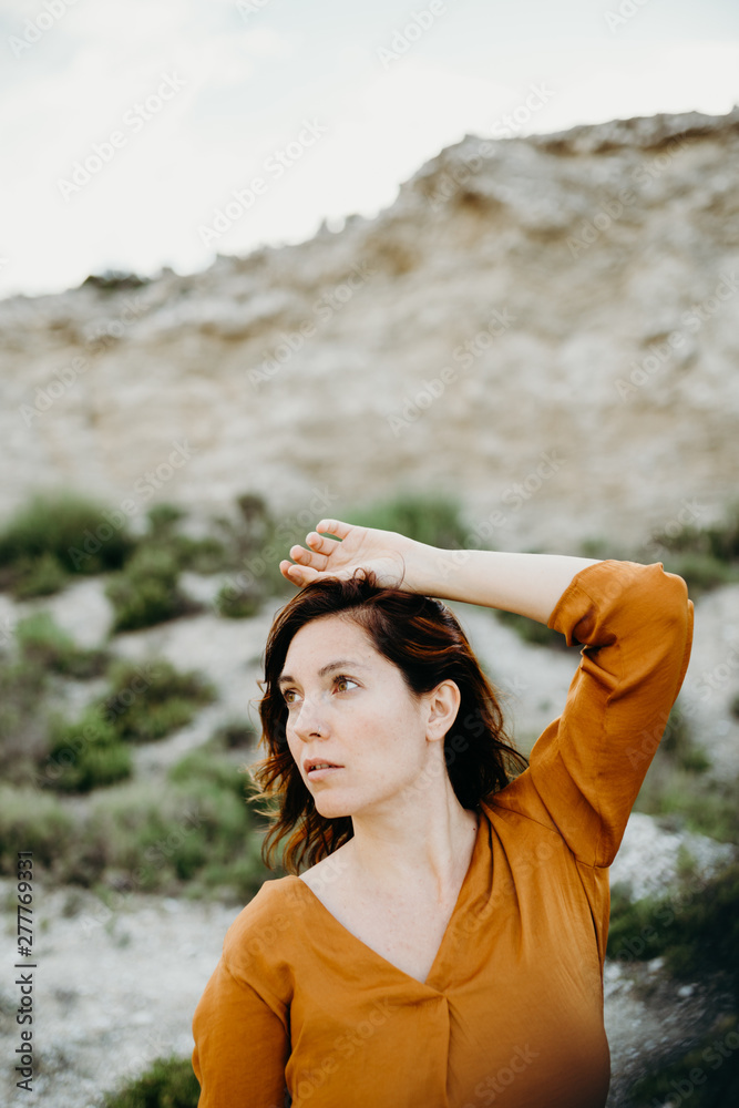 Portrait of thoughtful female model in blouse holding hand above head on  background of wild desert landscape Photos | Adobe Stock