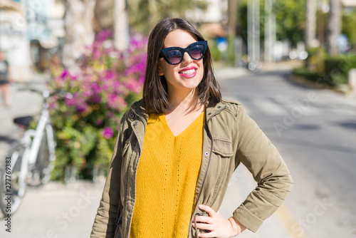 Beautiful young woman smiling cheerful walking on the street on a sunny day wearing sunglasses, casual pretty girl at the town