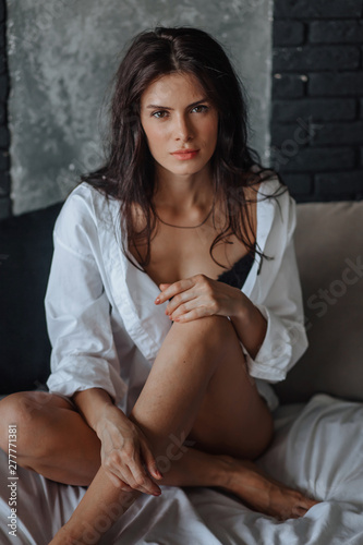 Sexy beautiful brunette girl with disheveled hair in black underwear on the bed. Portrait on dark background © Smeilov