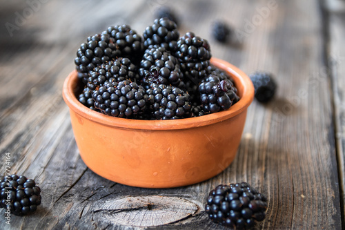 Fresh raw organic blackberries in a clay bowl on old wooden table