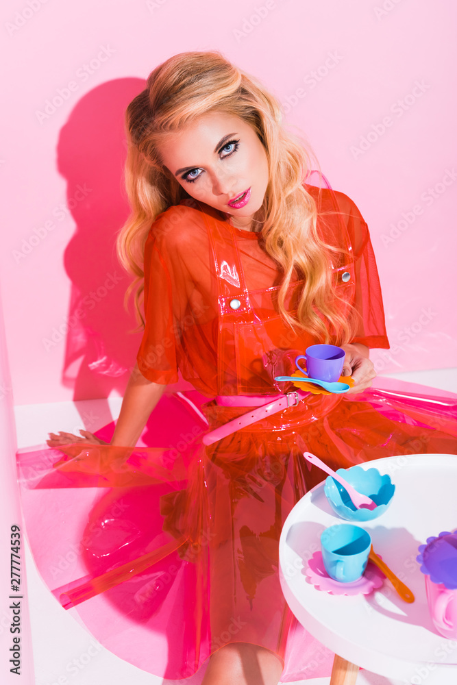 beautiful girl with toy cup looking at camera on pink, doll concept beautiful girl with toy cup looking at camera on pink, doll concept