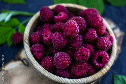 Fresh red ripe raspberries in a wooden cup on a dark background. Near green leaves. Red berries on a dark background.