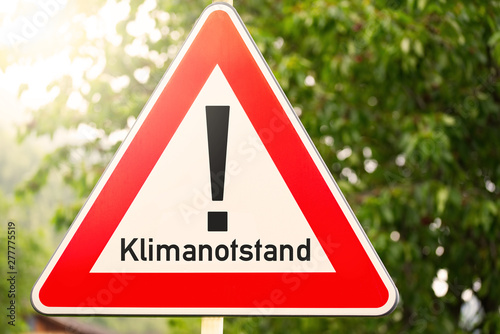 Achtung Schild mit Text Klimanotstand im Sonnenlicht vor grünem Hintergrund