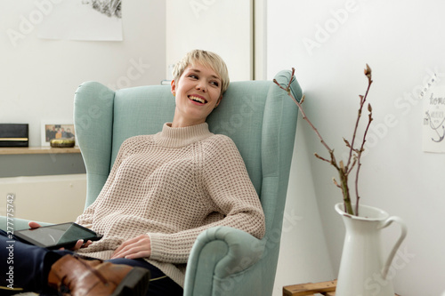 Happy woman sitting in armchair at home with tablet