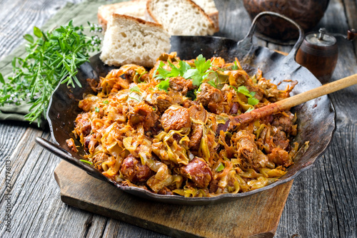 Traditional Polish kraut stew bigos with sausage, meat and mushrooms as closeup in a wrought-iron pan on an old wooden table photo