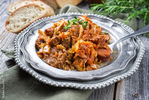 Traditional Polish kraut stew bigos with sausage, meat and mushrooms as closeup on a pewter plate on an old wooden table photo