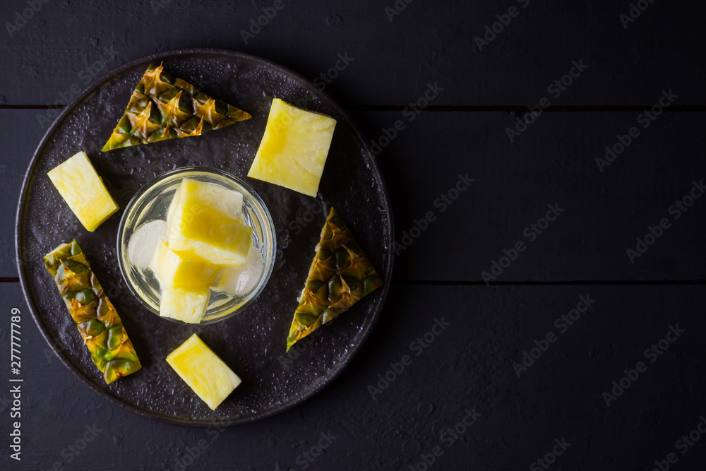 Pineapple on a dark background. Sliced pineapple on a black plate. Drink with ice and pineapple slices. Infused water. Copy space