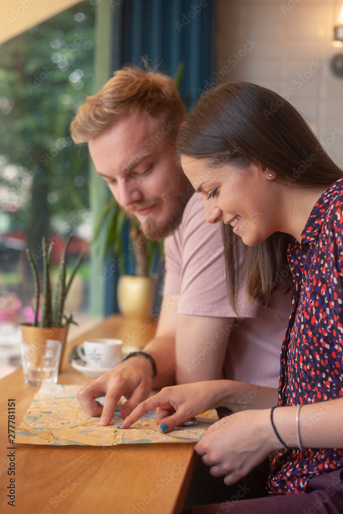 two smiling friends sitting together in cafe, happy while searching on a city map.