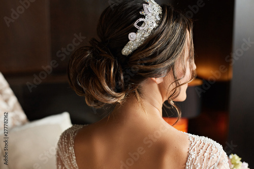 Wedding hairstyle with jewelry - fashionable brunette model young woman in a lace dress and with a diadem on her head before the wedding ceremony