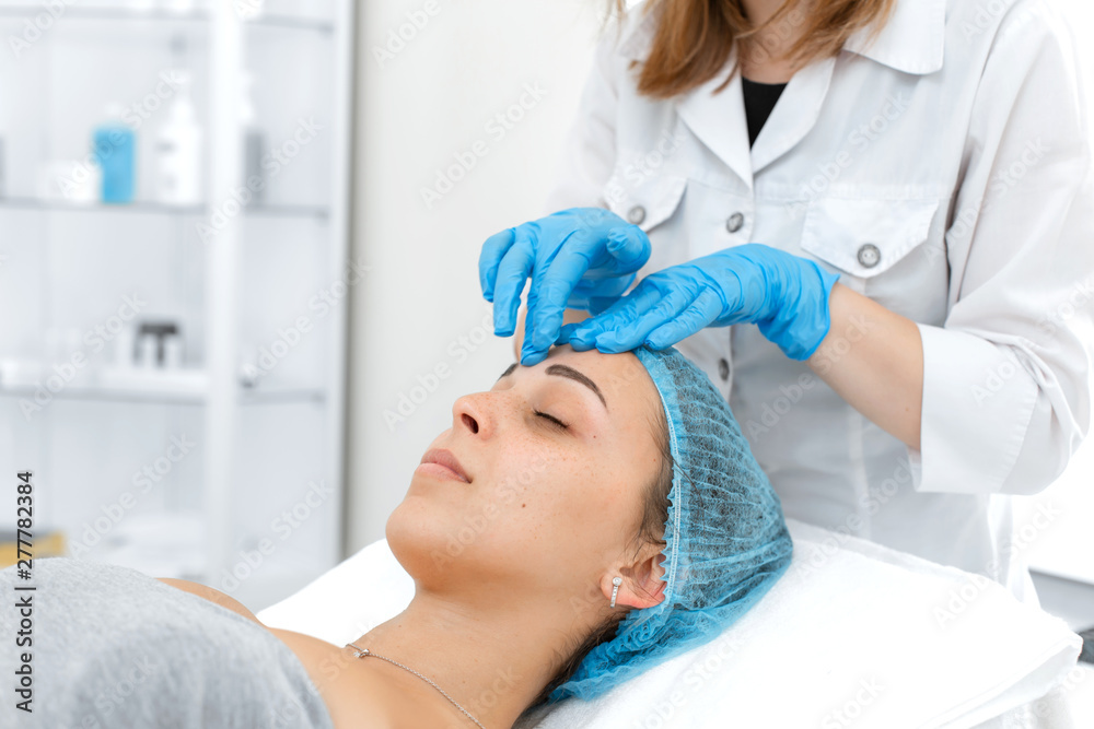 Beautician makes professional massage of the patient's face. A young girl is undergoing a course of spa treatments in the office of a beautician. Moisturizing, cleaning and facial skin care. Cosmetic