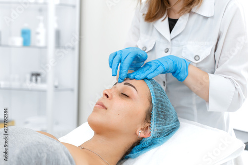 Beautician makes professional massage of the patient's face. A young girl is undergoing a course of spa treatments in the office of a beautician. Moisturizing, cleaning and facial skin care. Cosmetic