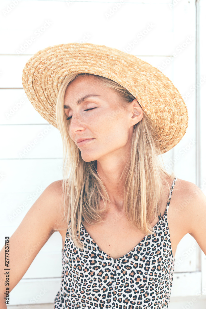 Profile portrait of a young authentic girl with freckles and square cheekbones. A woman in a straw hat and summer jumpsuit with leopard-patterned straps.