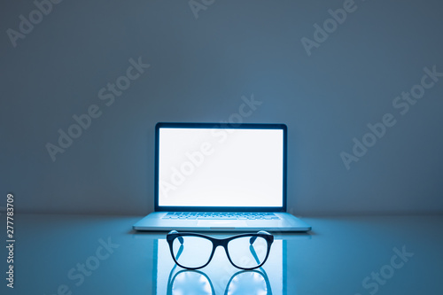 Computer eyeglasses in front of a laptop, low-key image. Blue light blockers and laptop in dark background, eye fatique problem concept photo