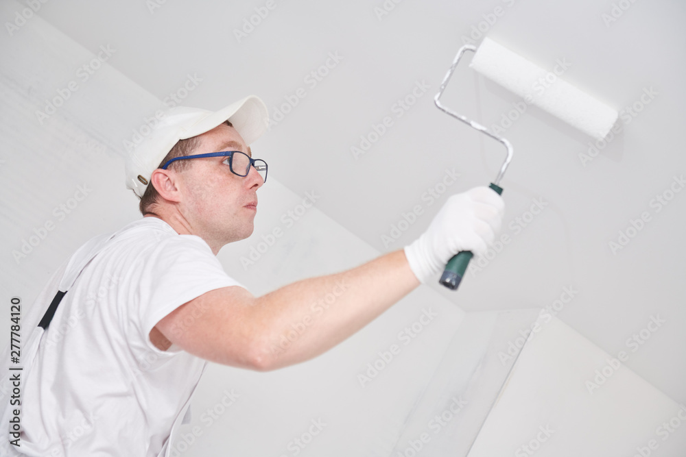 Painter worker with roller painting ceiling surface into white Painter worker with roller painting ceiling surface into white