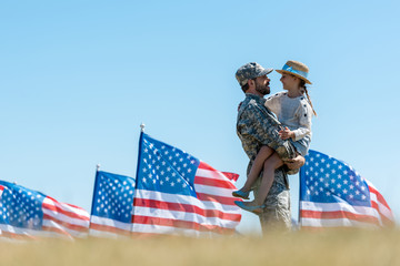 selective focus of man in military uniform holding in arms cheerful kid near american flags