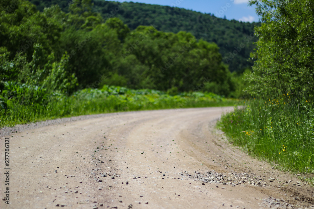 turn of a sandy stony road on a background of green trees and grass turn of a sandy stony road on a background of green trees and grass