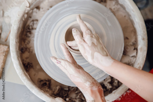 Top view of the potter wheel, hands of young woman make ceramic dishes from clay