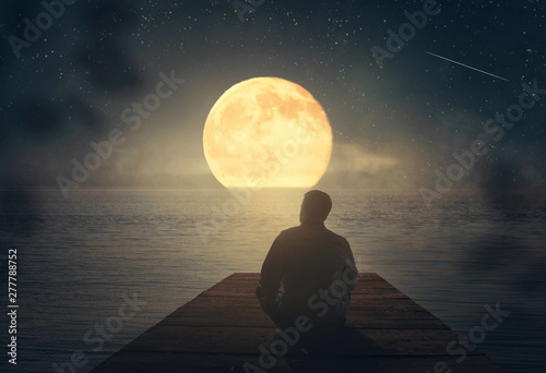 A man sits on the pier and looks at the moon.