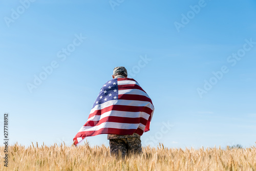 Back view soldier in cap and uniform holding American flag in field