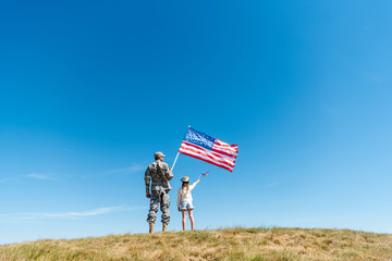 Back view of kid in straw hat and military father holding American flags