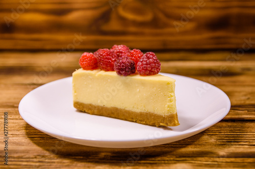 White plate with cheesecake New York and raspberries on wooden table