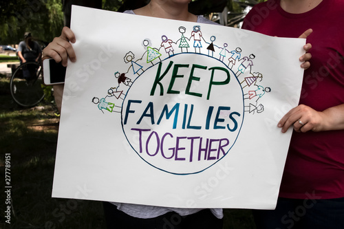 Two women at protest holding homemade sign together that says keep families together with world and families holding hands on it - cropped and selective focus
