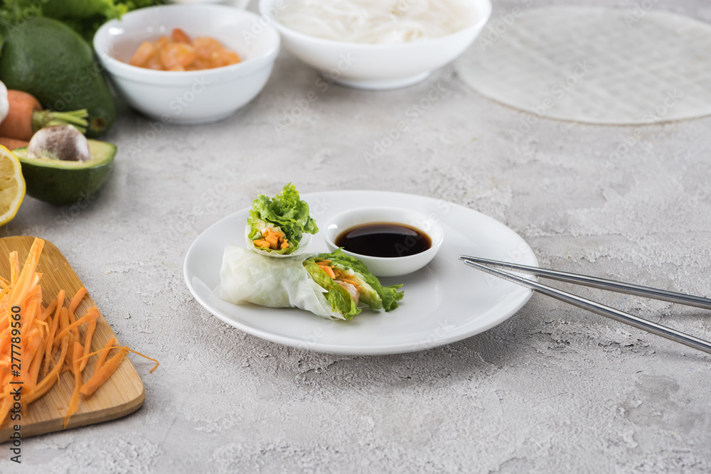 tasty and served spring rolls with soy sauce on white plate with metal sticks tasty and served spring rolls with soy sauce on white plate with metal sticks