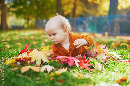 Girl sitting on the grass and playing with colorful autumn leaves