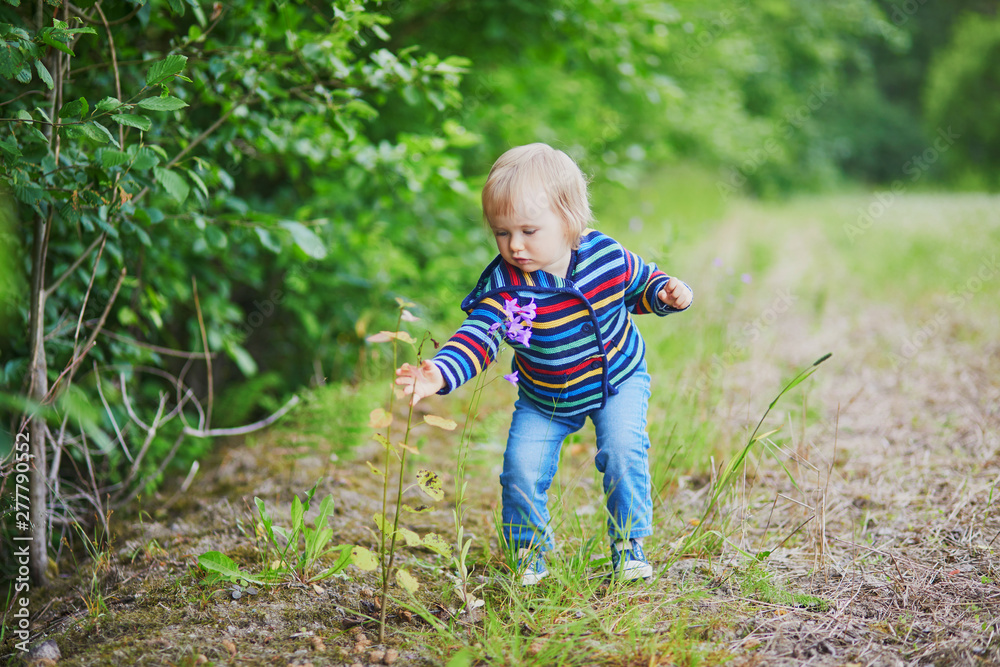 Adorable baby girl in the forest, looking at bell-flower Adorable baby girl in the forest, looking at bell-flower