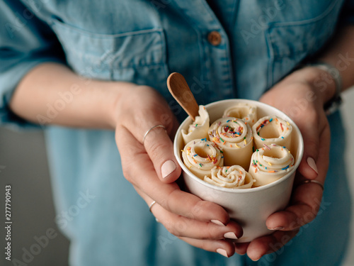 Rolled ice cream in cone cup in woman hands. Woman in jeans shirt holds cone cup with thai style vanilla rolled ice cream